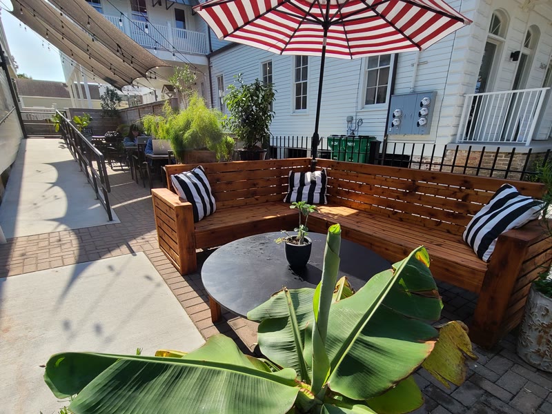 The wood corner bench on the Magazine Street patio, under the striped umbrella