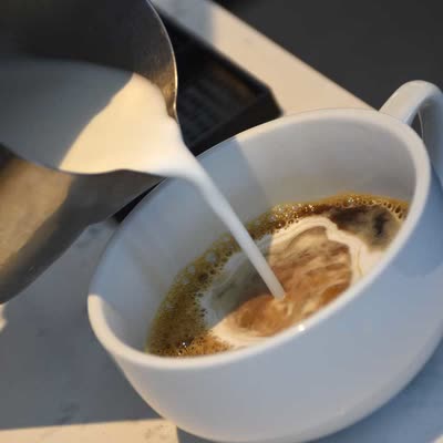 Steamed milk being poured into a cafe au lait in a white CR cup