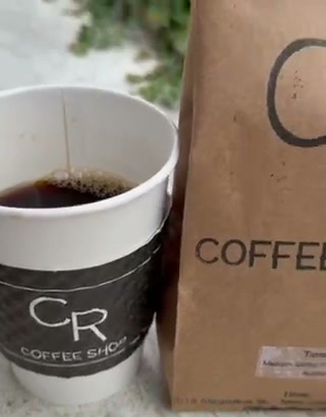 A CR Coffee Shop cup of fresh black coffee next to a brown CR Coffee Shop bag of roasted beans