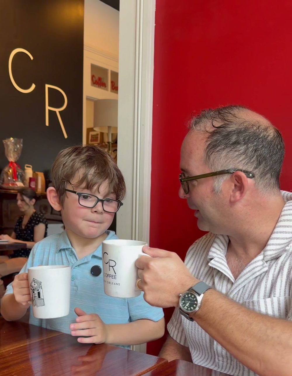 Kevin and Philip raising their white coffee mugs together over the table, about to drink