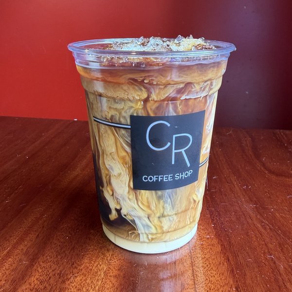 A cold brew over ice in a clear CR Coffee Shop cup, with dark coffee and milk swirled together through the cup
