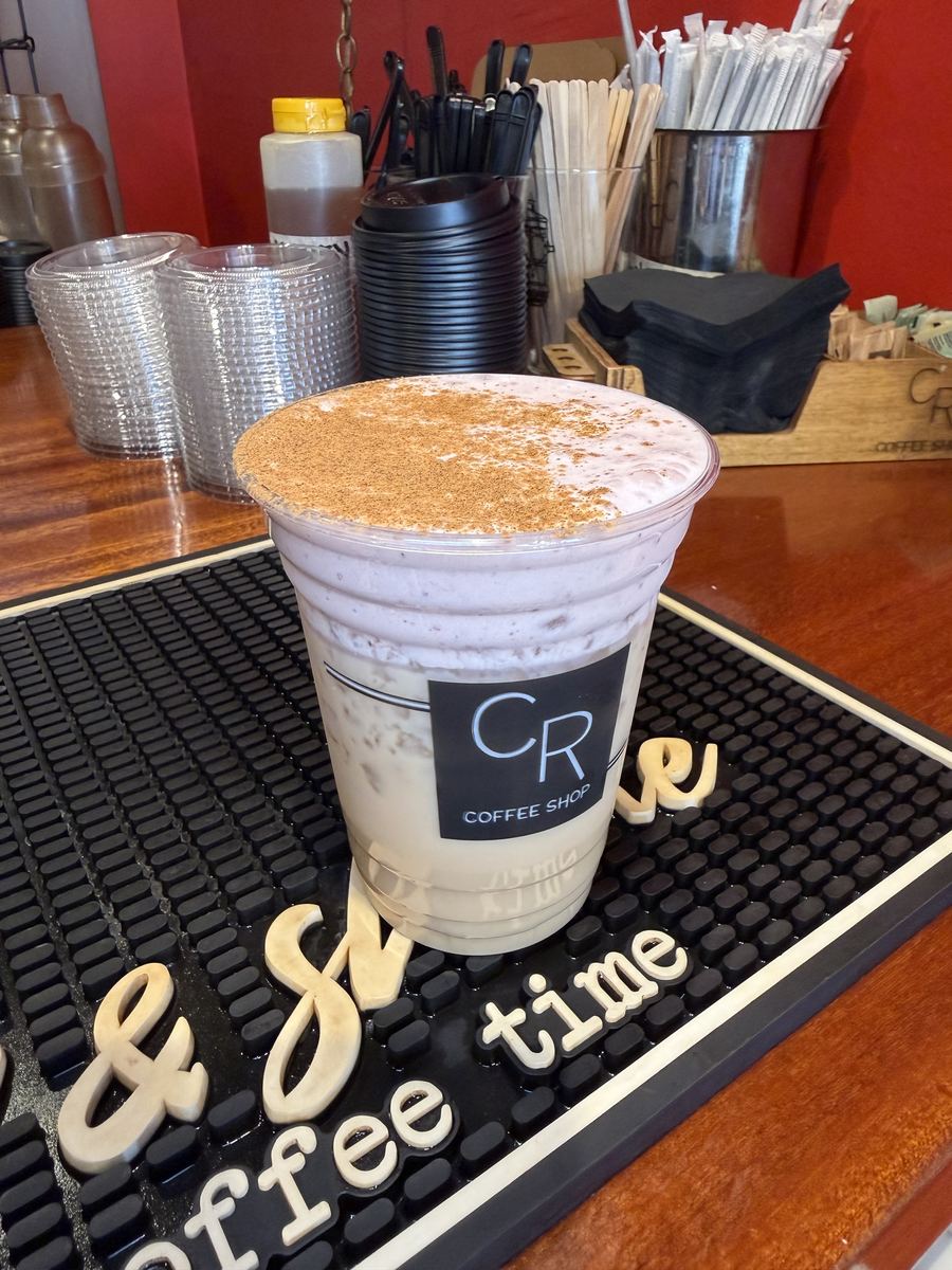 CR Coffee Shop iced Strawberry Chai with cinnamon dusted on top, sitting on a black bar mat at the Magazine Street counter