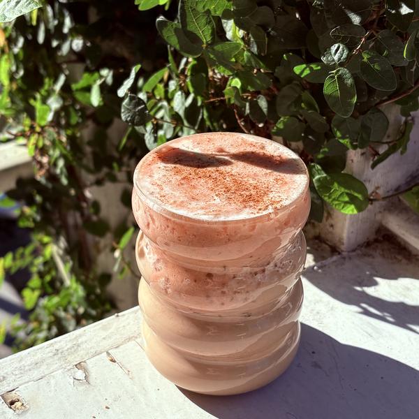 Iced Strawberry Chai dusted with cinnamon, sitting on a sunlit patio railing surrounded by green leaves